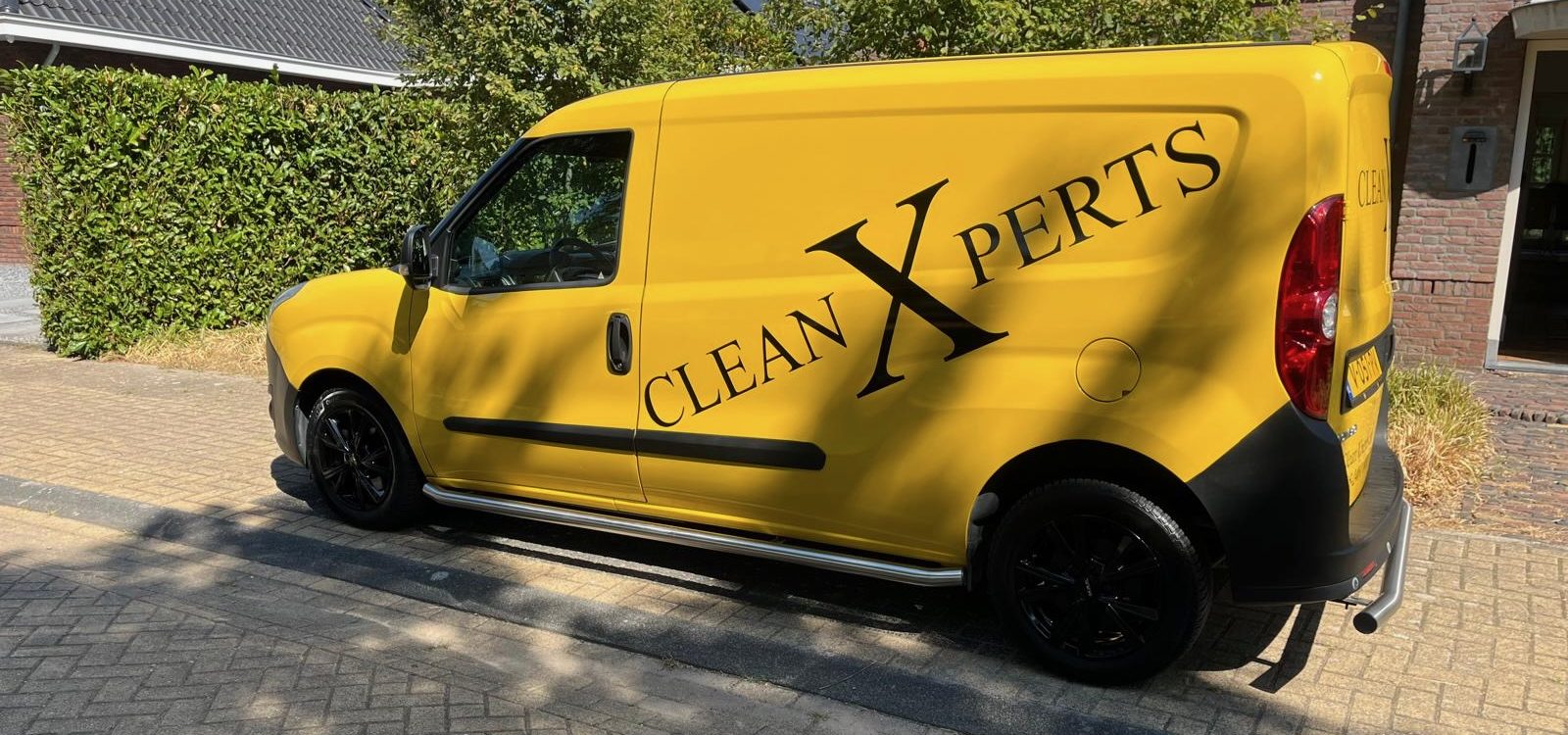 Gele bedrijfsbus van glazenwasserij CleanXperts geparkeerd in een woonstraat in Uden